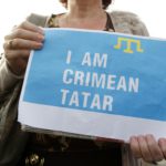 Людина із саморобним плакатом, на якому зображений кримськотатарський прапор та напис англійською мовою: I am crimean tatar.