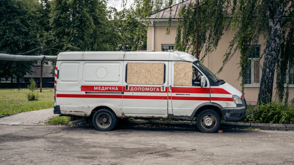 Карета швидкої допомоги (вид збоку) - на авто видно вм'ятини, замість вибитих вікон встановлено фанеру