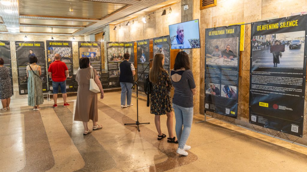 Група з семи людей роздивляється плакати з фото та історіями військовополонених та їхніх сімей.