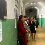 Група людей стоїть вздовж стіни, на якій розміщені фото експозиції "Оглушлива тиша"