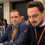 Сулейман Мамутов сидить за столом та говорить у мікрофон, поруч - ще двоє осіб. На задньому плані - слухачі виступу.