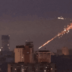 Вид на нічне місто здалеку. Вибух ракети над будинками супроводжується багатьма спалахами та слідом від падіння уламків.