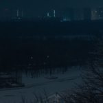 Вид на житловий мікрорайон здалеку. В кадрі видно силуети будинків, що поринули в темряву, подекуди у вікнах видно тьмяне світло.